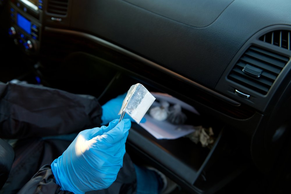 A gloved hand uses tongs to hold a bag of white powder.
