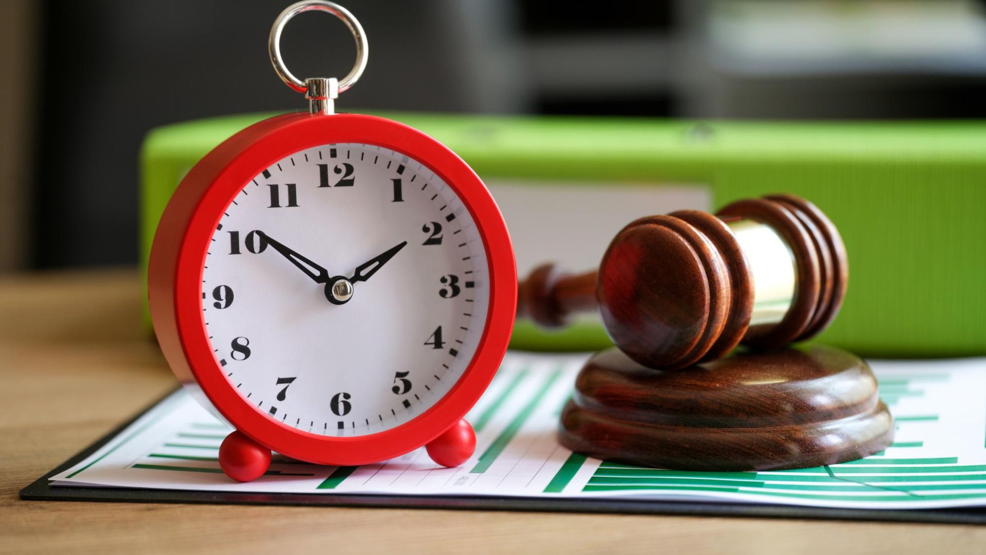 A red alarm clock and a judge's gavel rest on legal documents with green charts, symbolizing legal deadlines and court proceedings
