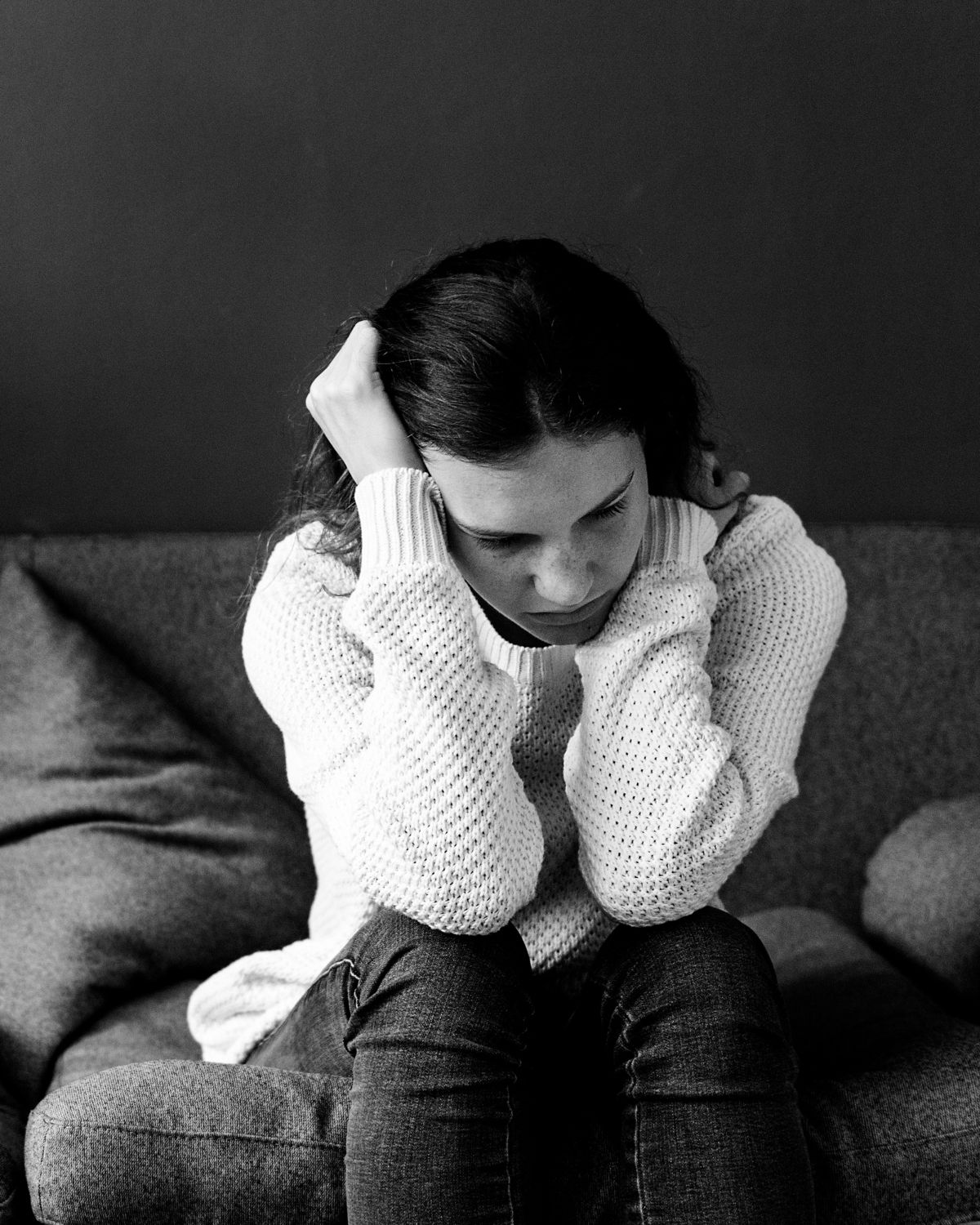A black and white image shows a young woman sitting on a couch