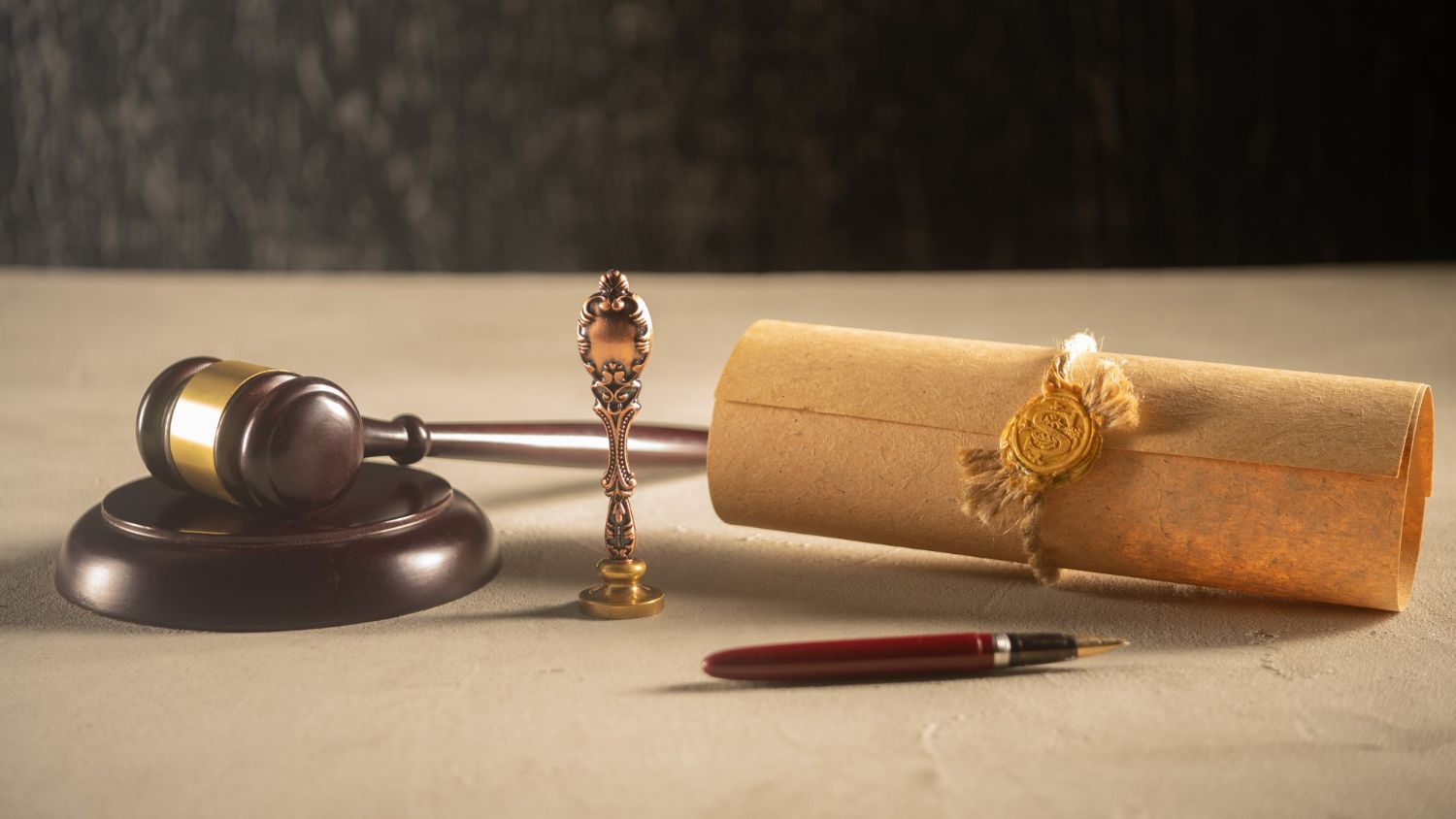 A gavel, decorative seal, and scroll with a wax seal are arranged on a desk