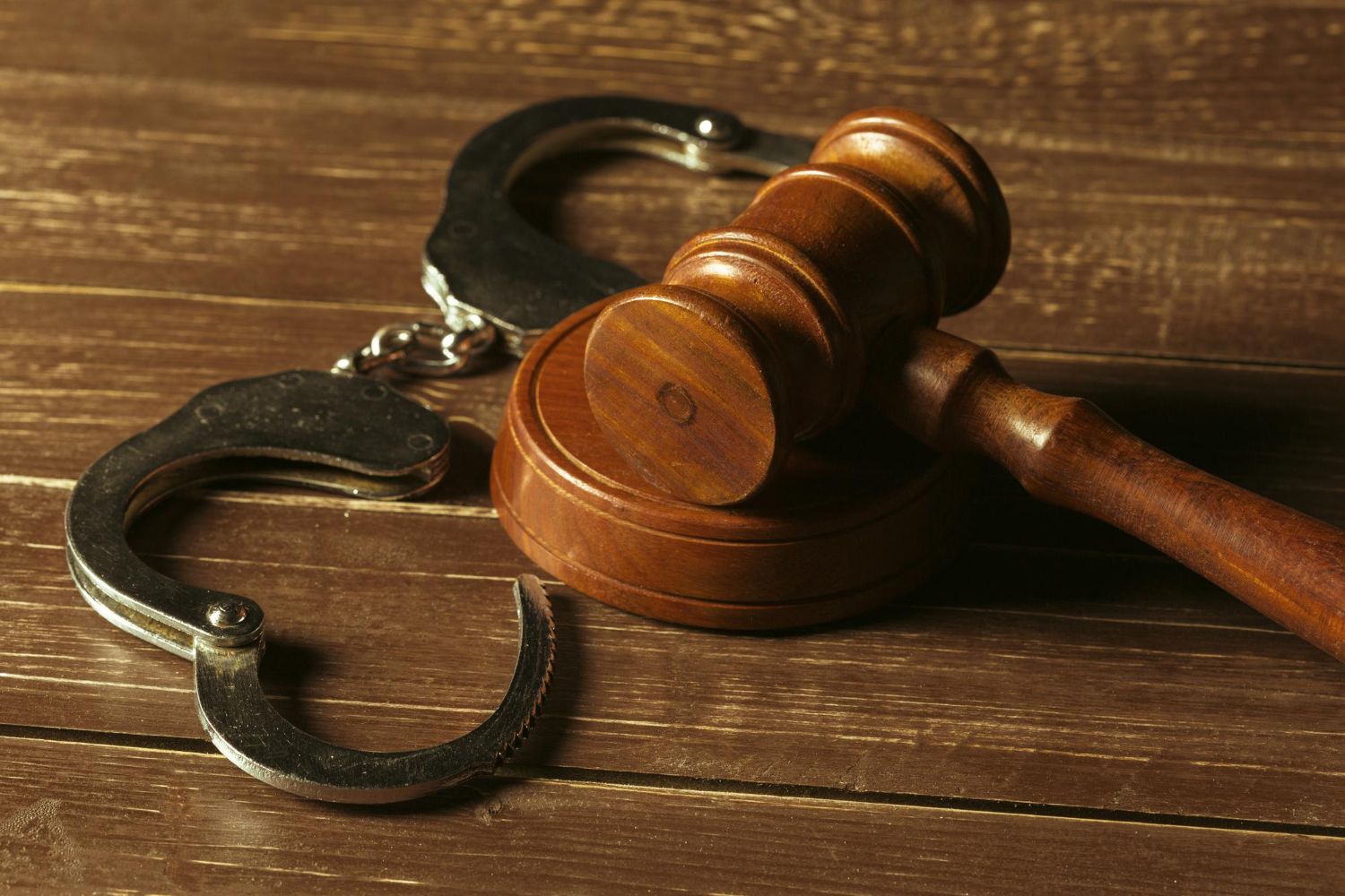 Silver handcuffs and a wooden gavel rest on a dark wooden surface