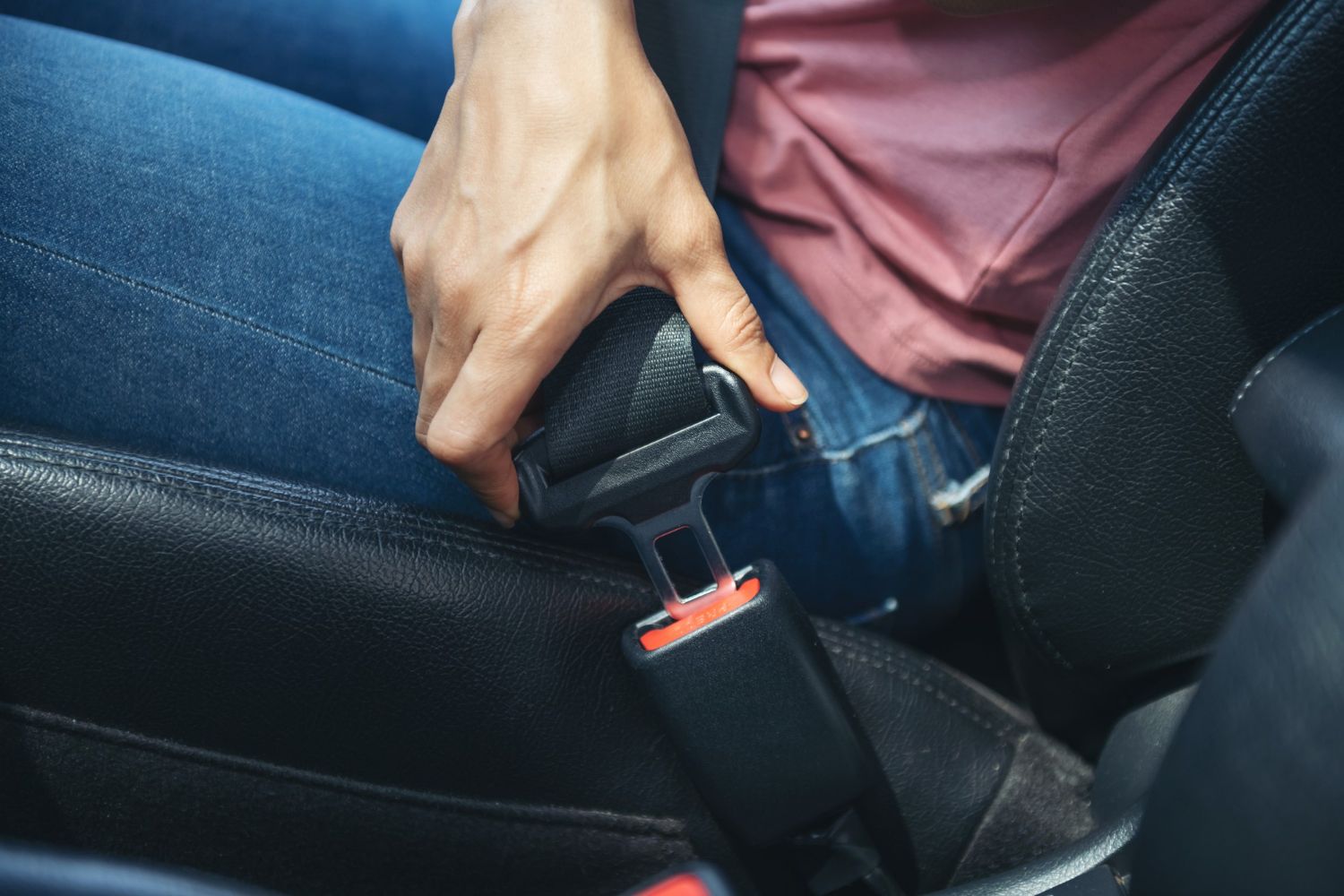 A person's hand buckles a car seatbelt, inserting the buckle into the black latch