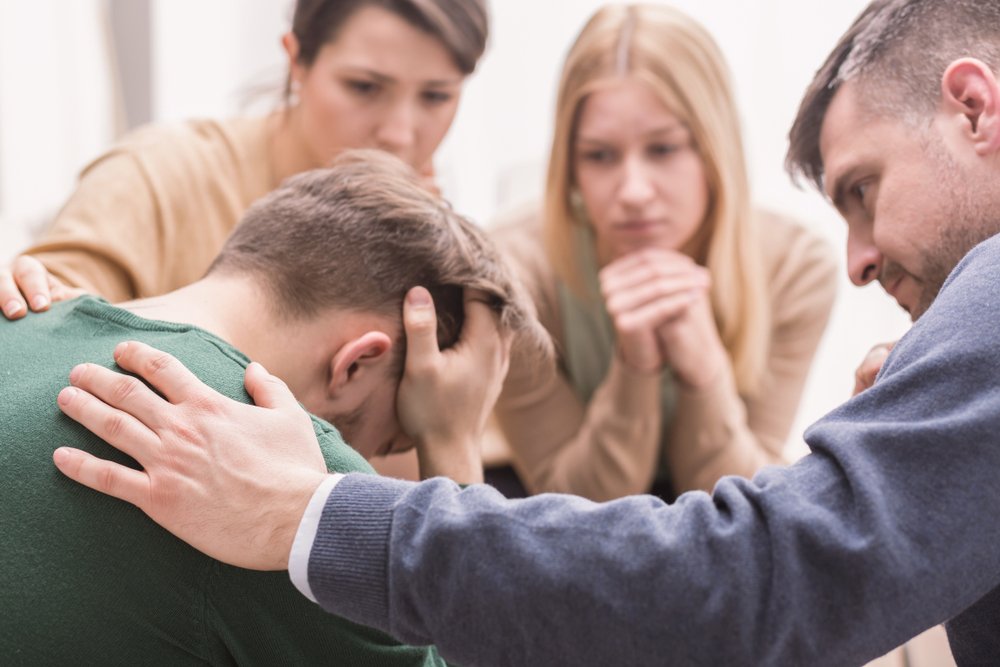 A group of four individuals offers comfort to a distressed man