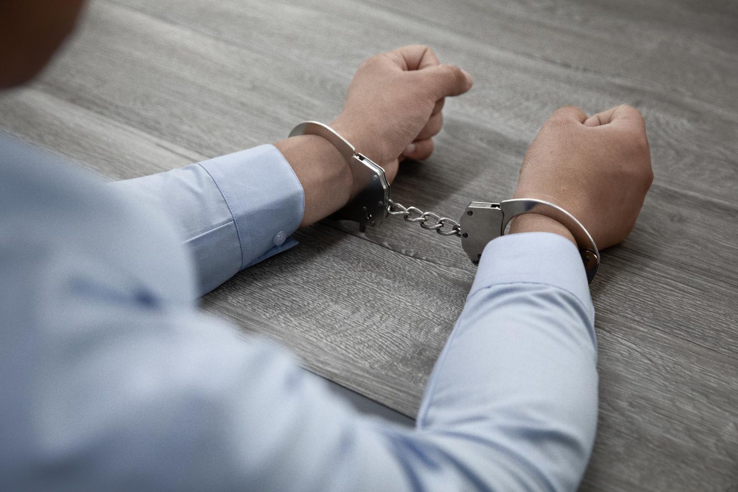 selective-focus-shot-male-hands-handcuffs-wooden-table.jpg Name: selective-focus-shot-male-hands-handcuffs-wooden-table