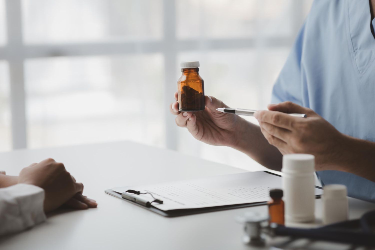 A person holds a brown bottle and points with a pen during a consultation