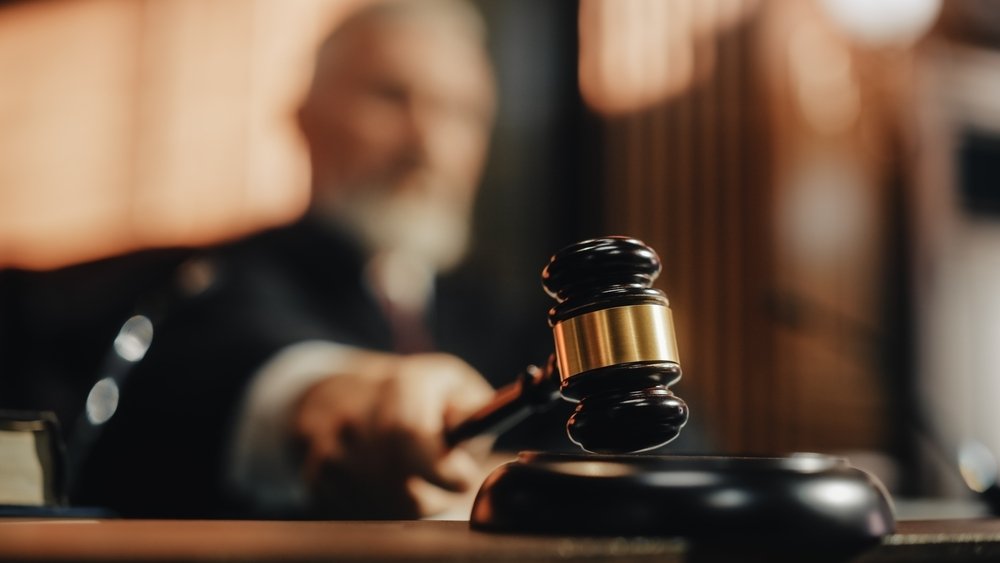 A judge's hand holds a gavel, poised to strike a sound block.
