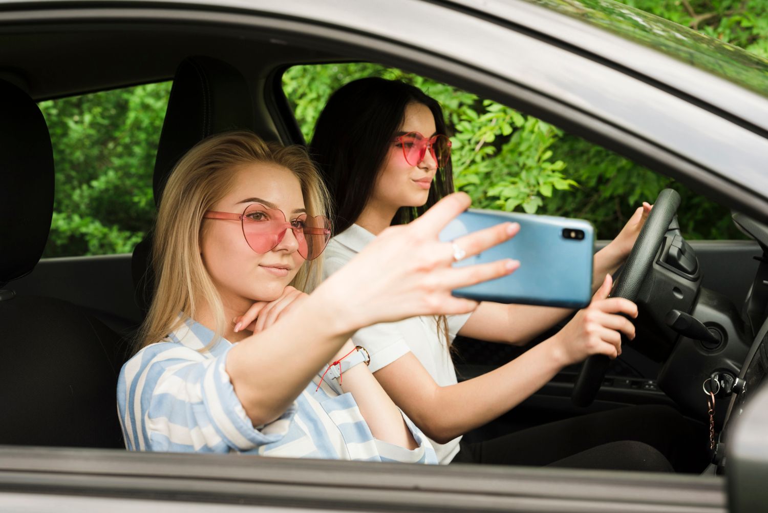 A blonde woman in the passenger seat takes a selfie with a phone