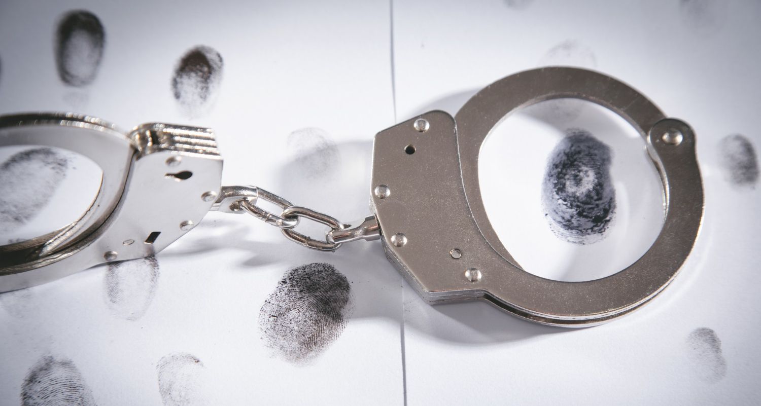 A pair of silver handcuffs rests on a white background marked with numerous black fingerprints