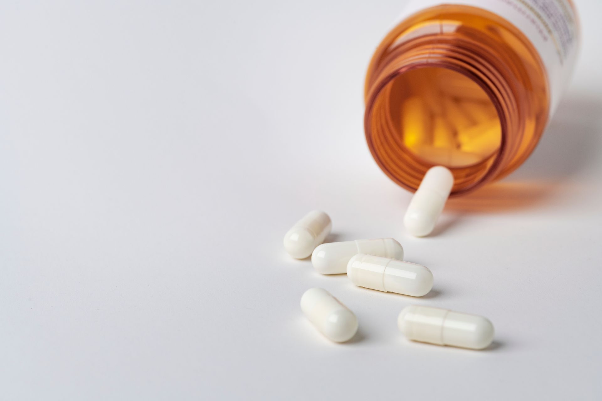 White capsules spill from an orange prescription bottle onto a white surface
