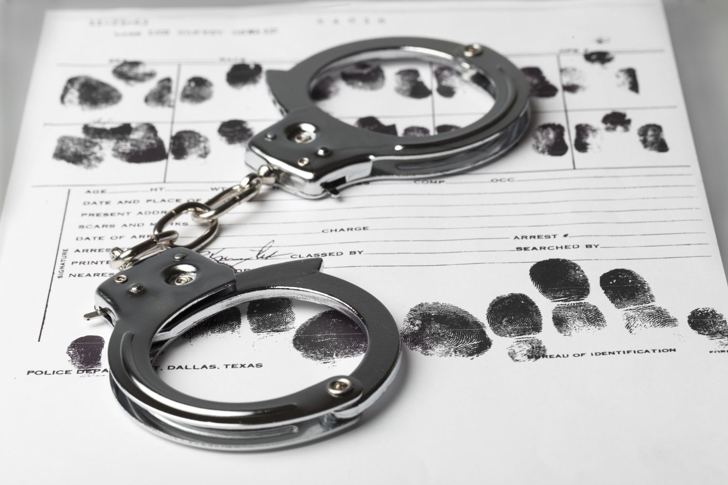Silver handcuffs lie on a police identification form covered in black fingerprints.