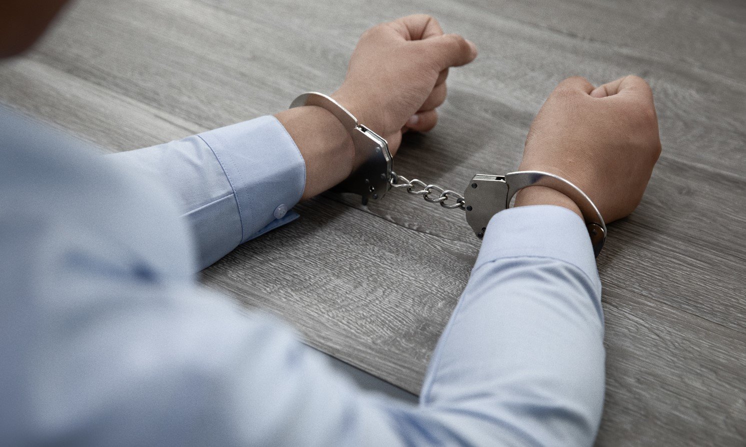 A person's wrists are handcuffed on a light gray table