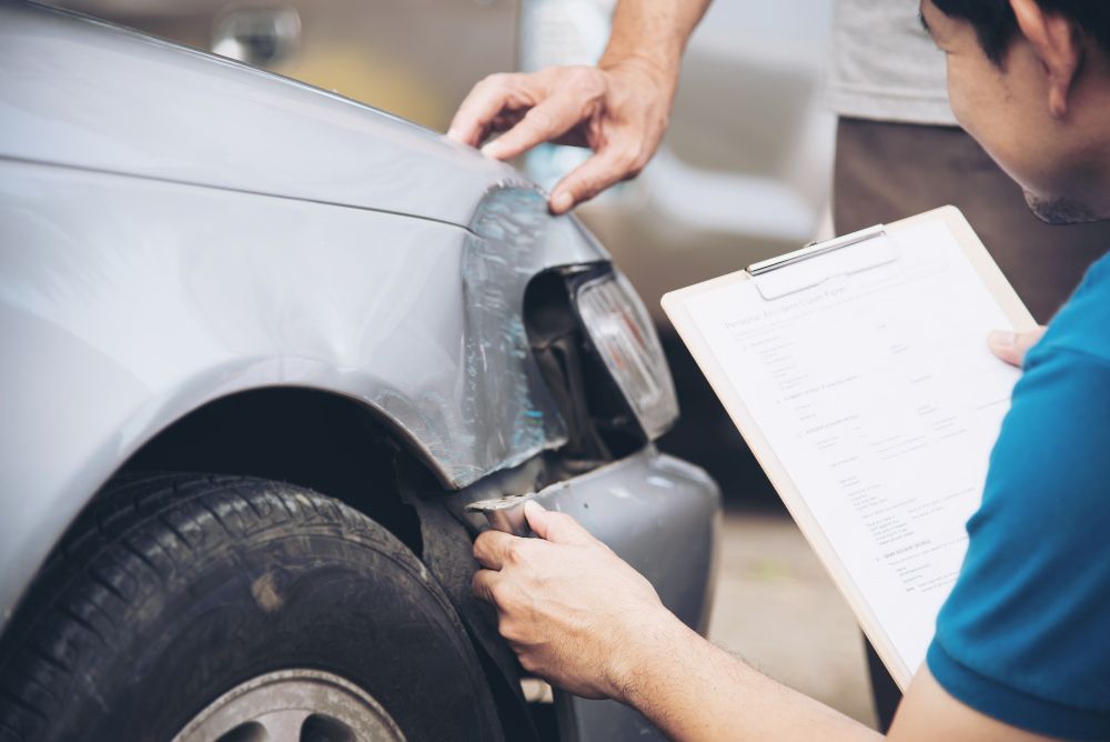 Two people inspect a damaged car's fender