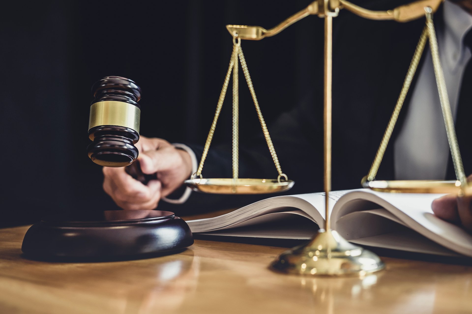 A hand holds a gavel mid-air over a desk with legal scales