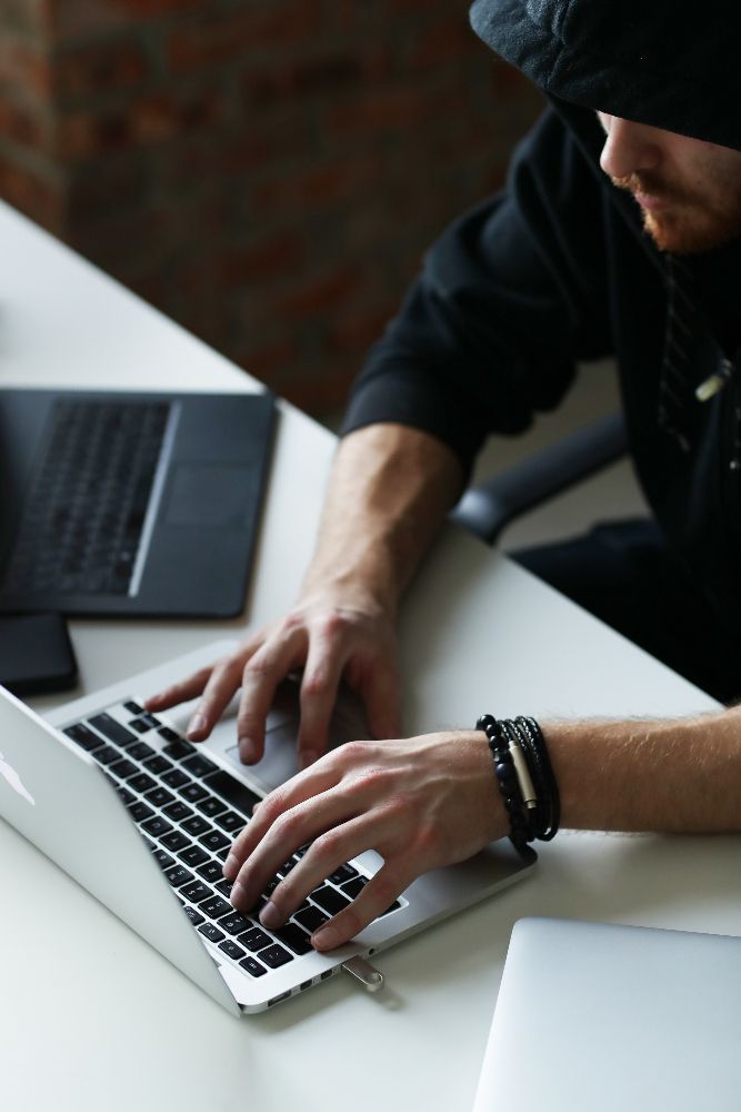 A person in a black hoodie types on a silver laptop