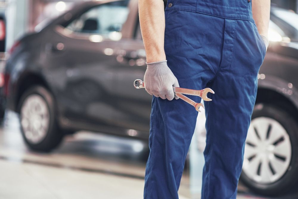 A mechanic in blue overalls holds two wrenches