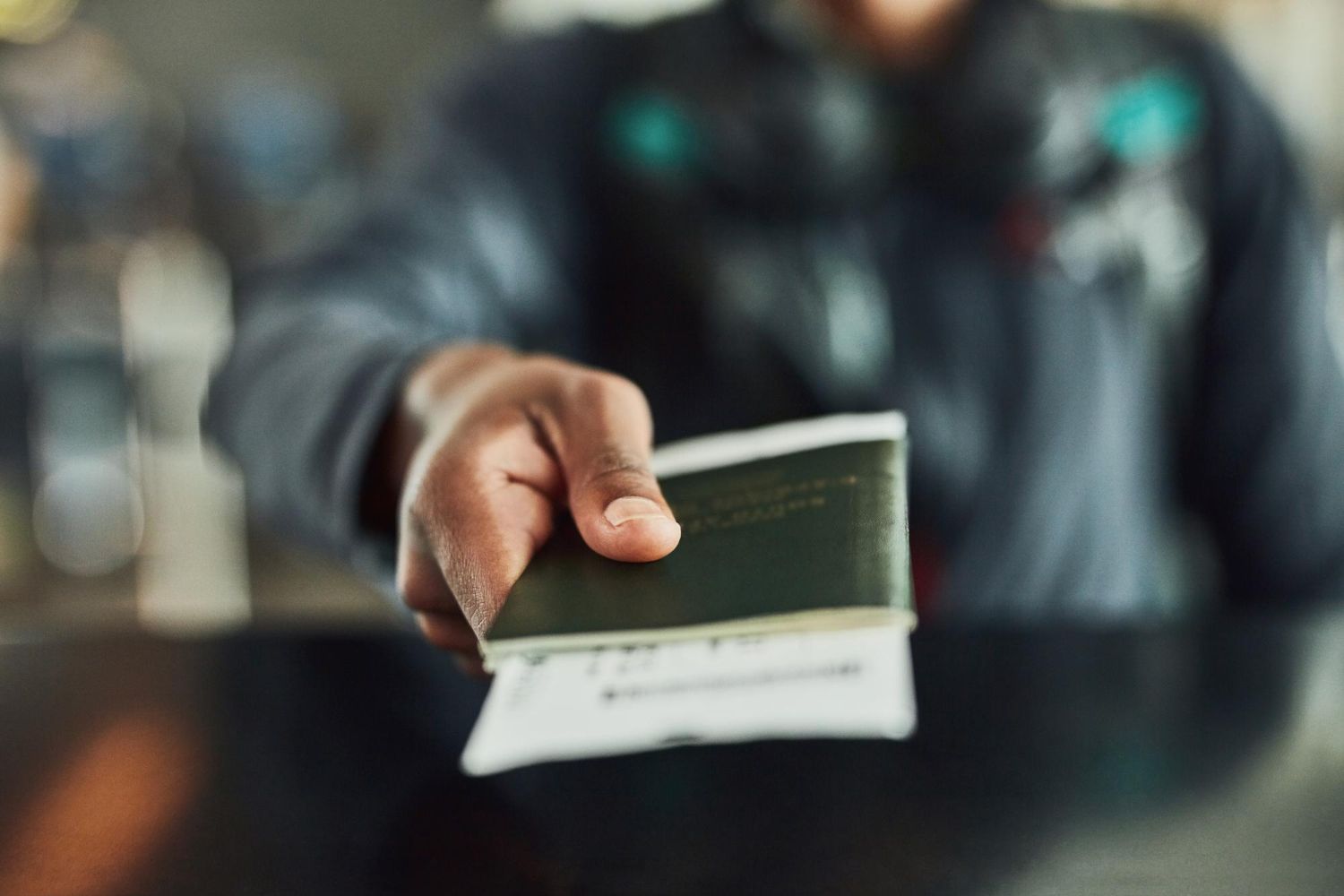 A person's hand extends a dark green passport and travel ticket forward