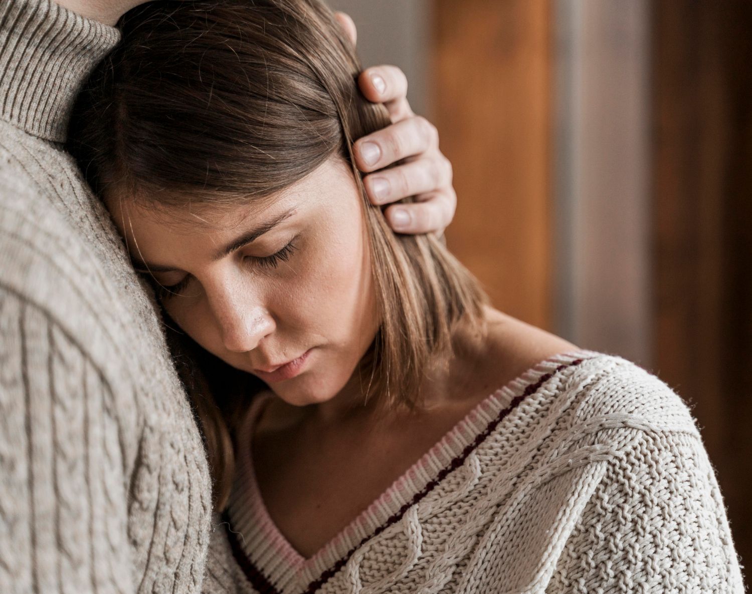 A young woman with closed eyes rests her head on a man's shoulder