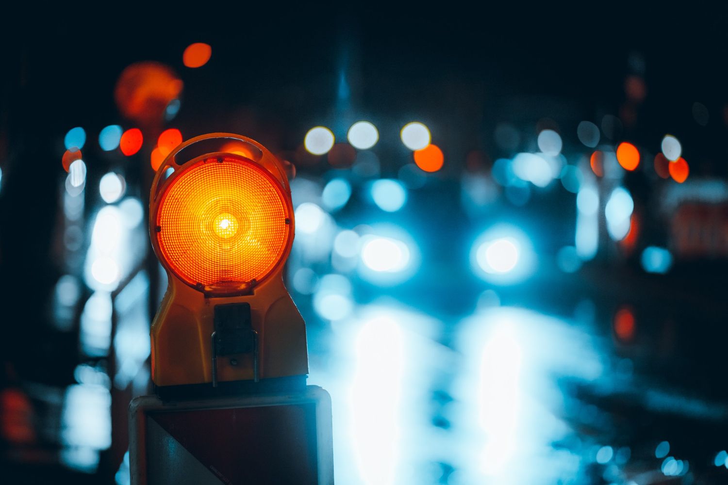A glowing orange warning light stands on a dark, wet road at night